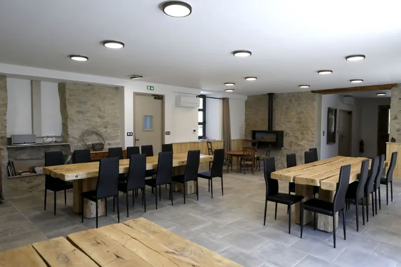 Grande salle de réception avec poutres apparentes, poêle à bois et murs en pierre