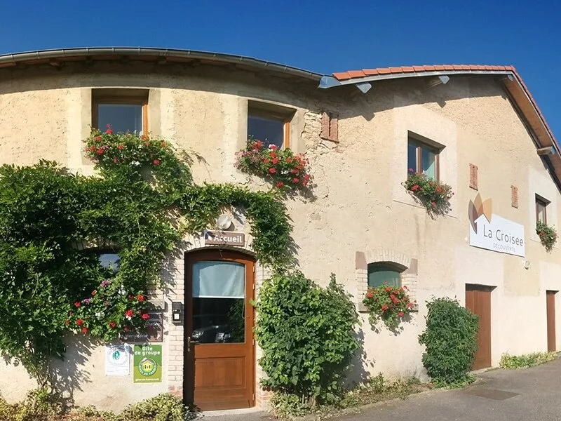 Gîte de groupe La Croisée Découverte à Reillon — Façade en pierre de l'ancienne ferme avec géraniums aux fenêtres et enseigne du gîte, capacité 48 personnes