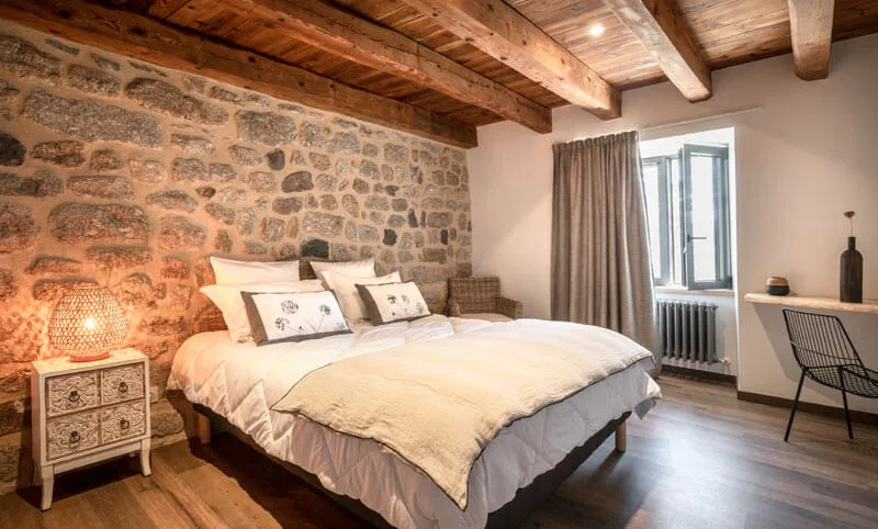 Chambre avec grand lit, mur en pierre et poutres apparentes