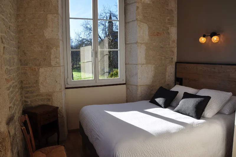 Chambre voûtée en pierre avec lit double et fenêtre donnant sur le clocher du village