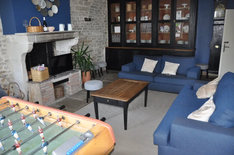 Grand salon avec cheminée en pierre, baby-foot, bibliothèque et canapés bleus