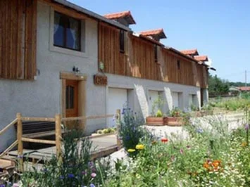 Gîte de groupe Les Gîtes de la Verrerie de Portieux à Portieux — Façade en bois et pierre du gîte avec jardin fleuri et terrasse en bois, capacité 32 personnes