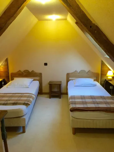 Chambre mansardée avec deux lits jumeaux sous charpente en bois