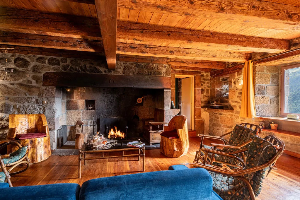 Salon avec grande cheminée en pierre, fauteuils rustiques et canapés bleus