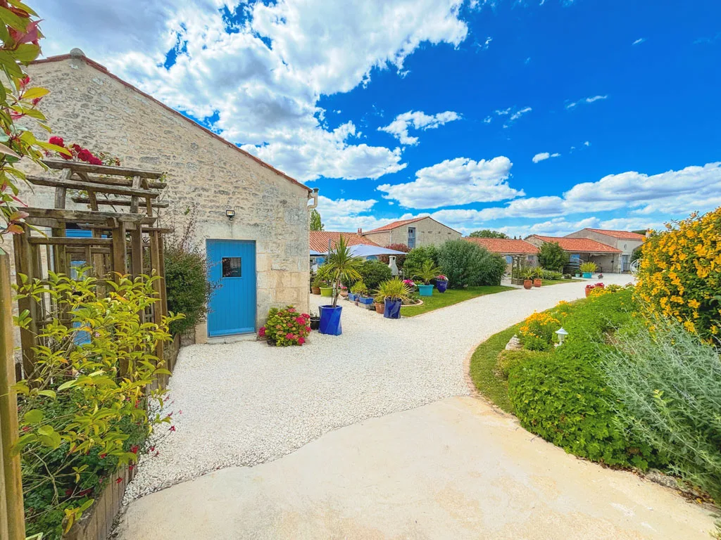 Allée fleurie du domaine avec porte bleue et massifs colorés