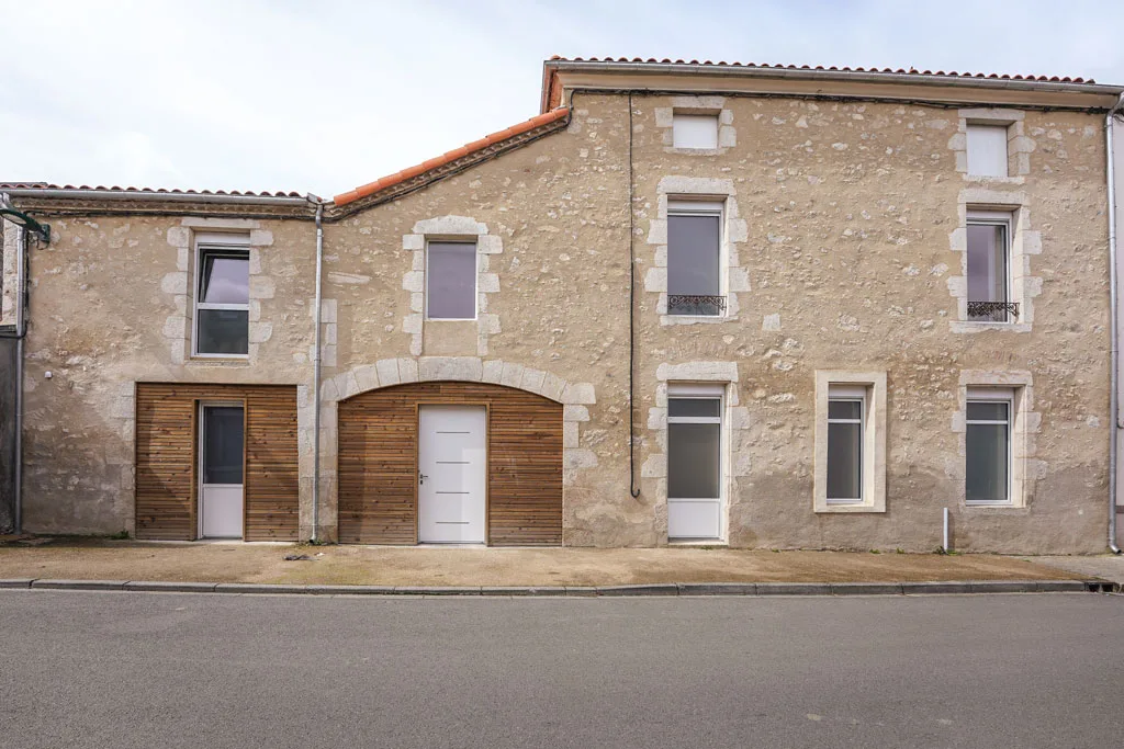 Façade en pierre de la maison de village avec grandes fenêtres et porte en bois