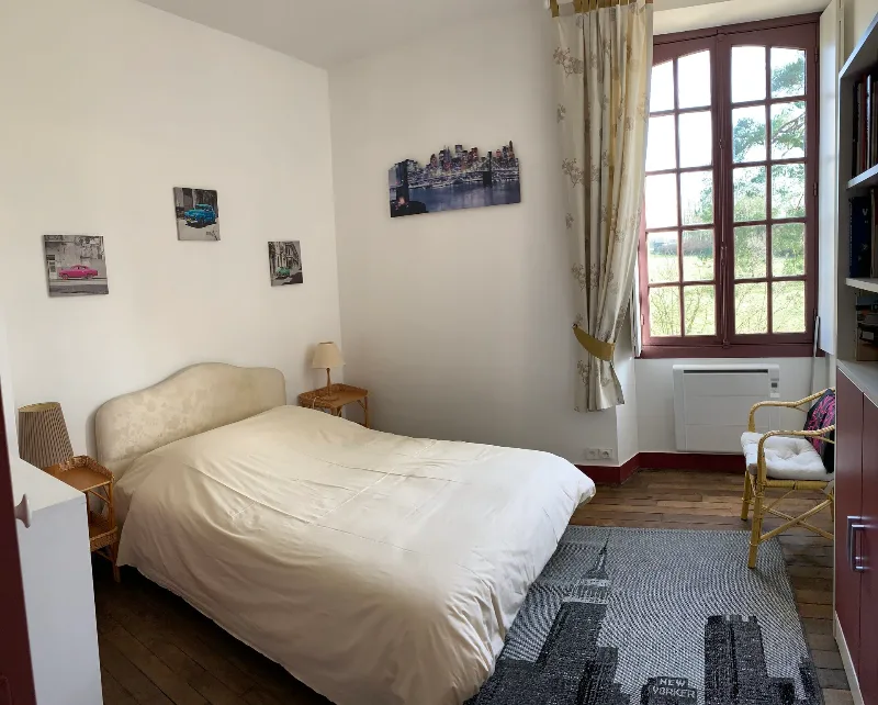 Chambre avec lit double, poutres apparentes et fenêtre donnant sur la campagne