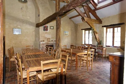 Grande salle commune sous charpente en bois avec plusieurs tables et cheminée en pierre