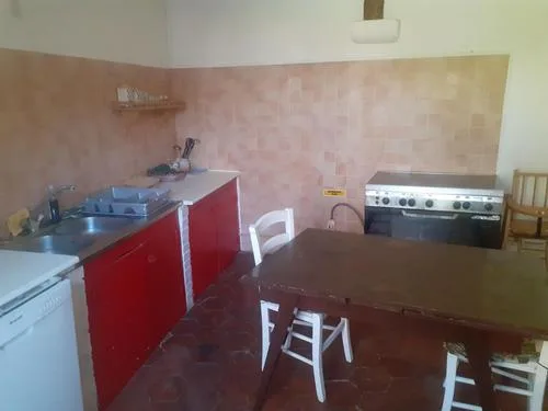 Cuisine équipée avec meubles rouges, évier, plaques de cuisson et grande table en bois