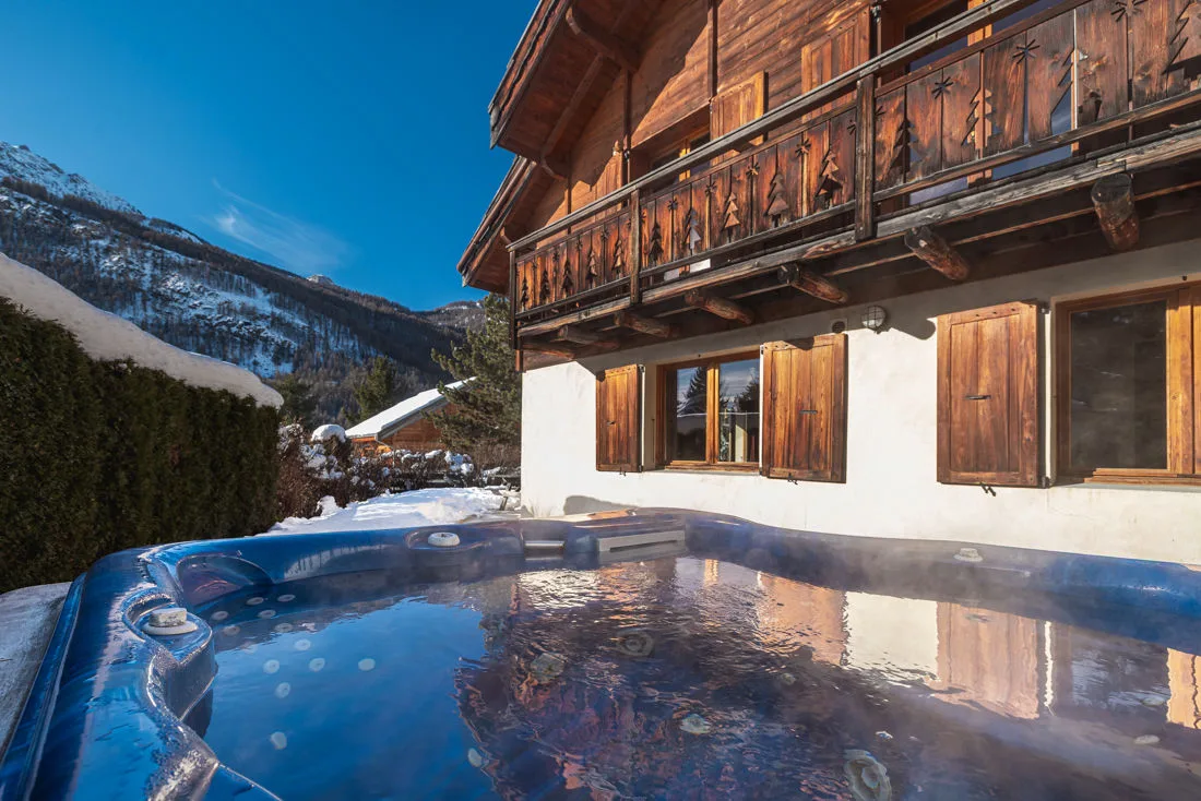 Spa extérieur fumant devant la façade enneigée du chalet