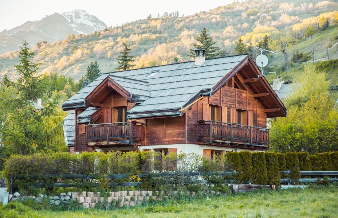 Façade du chalet en bois entourée de verdure au printemps avec vue sur les sommets