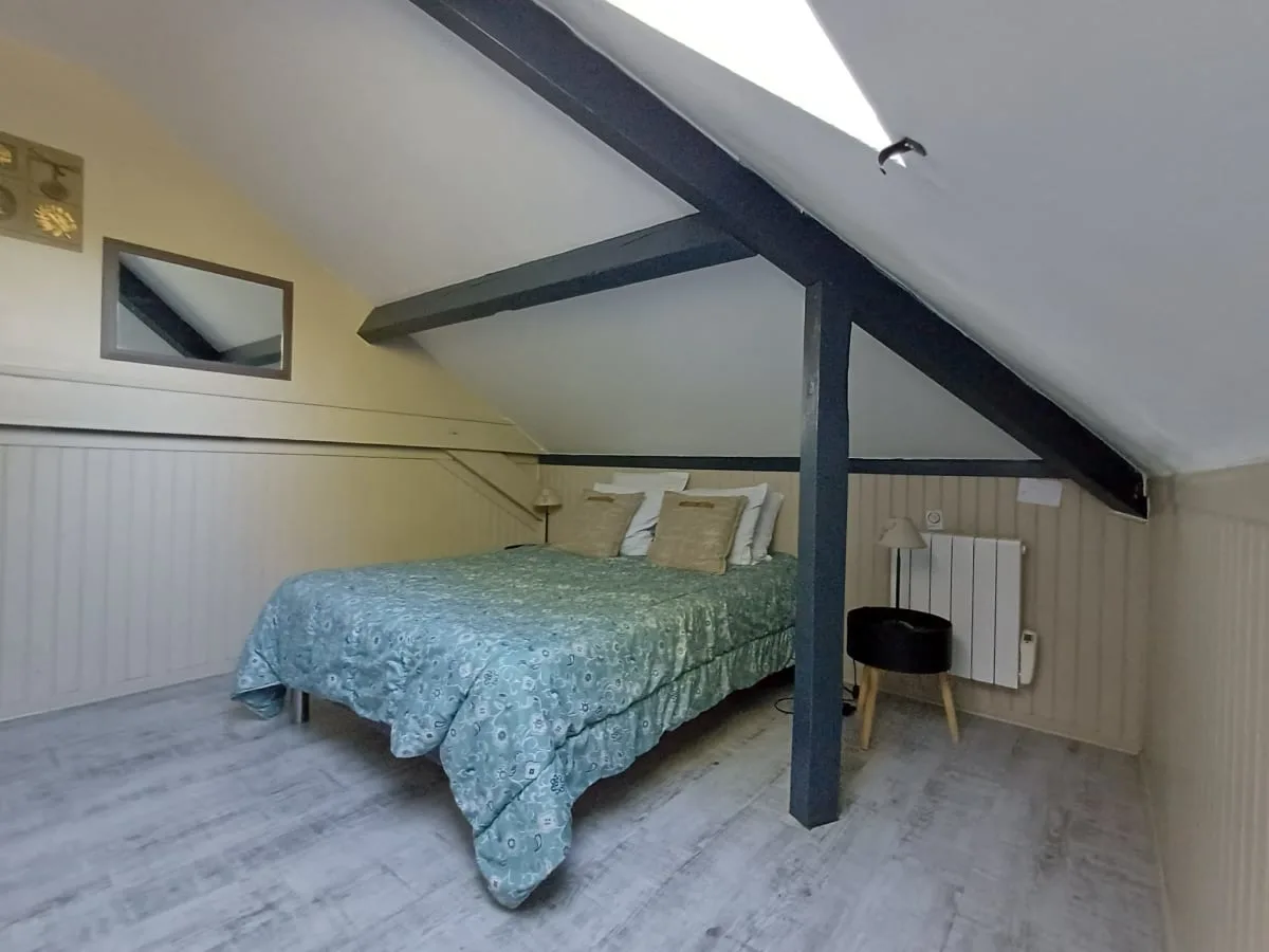 Chambre mansardée avec lit double, poutres apparentes et velux au plafond
