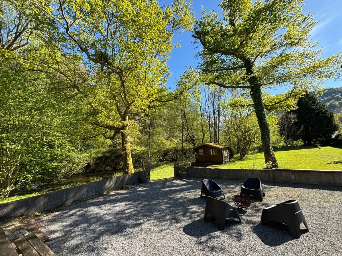 Jardin du gîte avec cabanon en bois, grands arbres et ruisseau en contrebas
