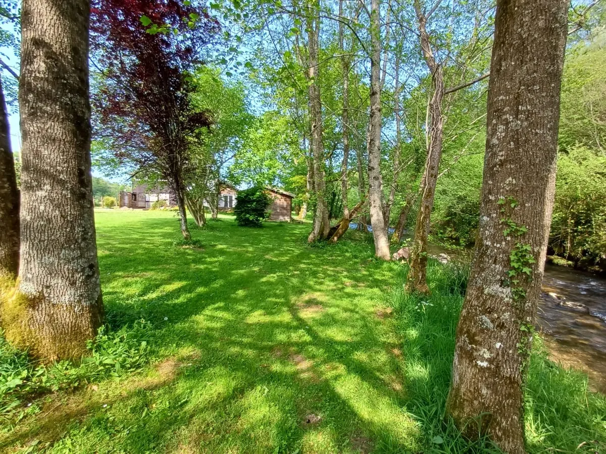Terrain gravillonné avec fauteuils noirs autour d'un brasero, façade du gîte en arrière-plan