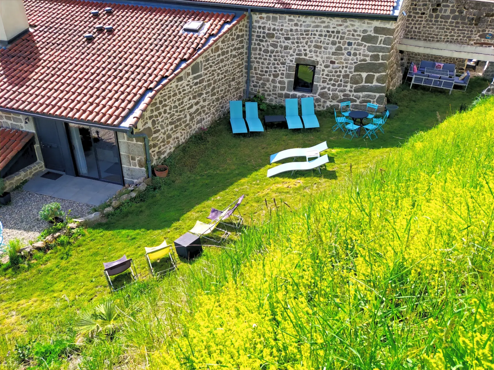 Grand jardin fleuri en pente avec transats bleus et mobilier de jardin coloré