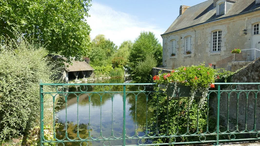 La maison vue depuis le pont sur l'Aigre, jardinière fleurie au premier plan