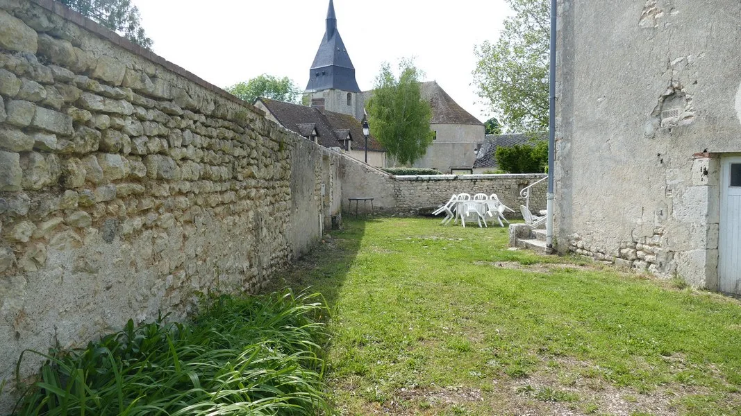 Cour en pierre avec table et chaises, clocher de l'église en arrière-plan