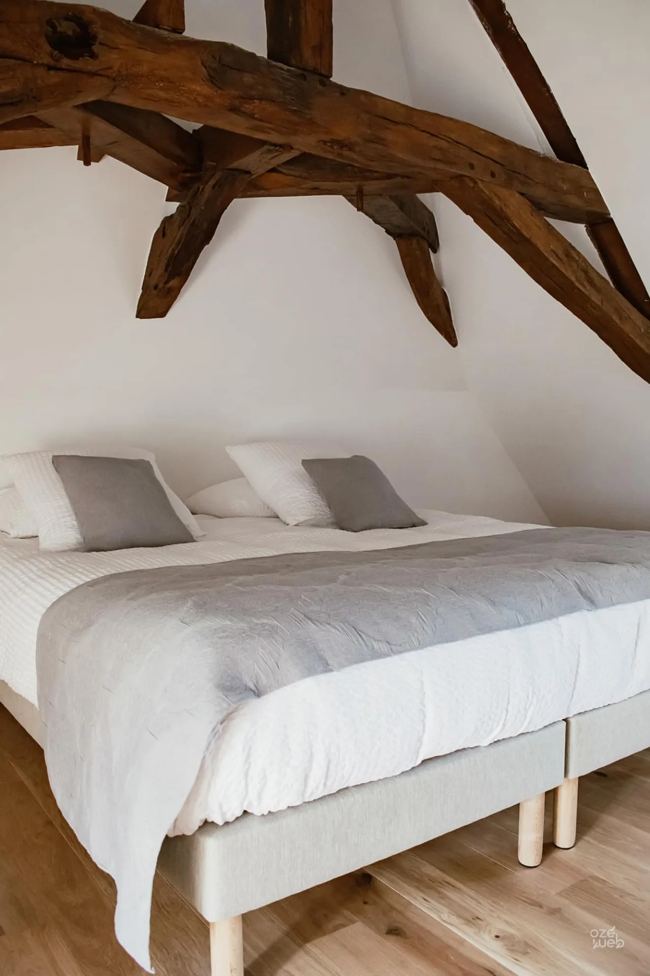 Chambre mansardée sous charpente apparente avec poutres anciennes et lit double