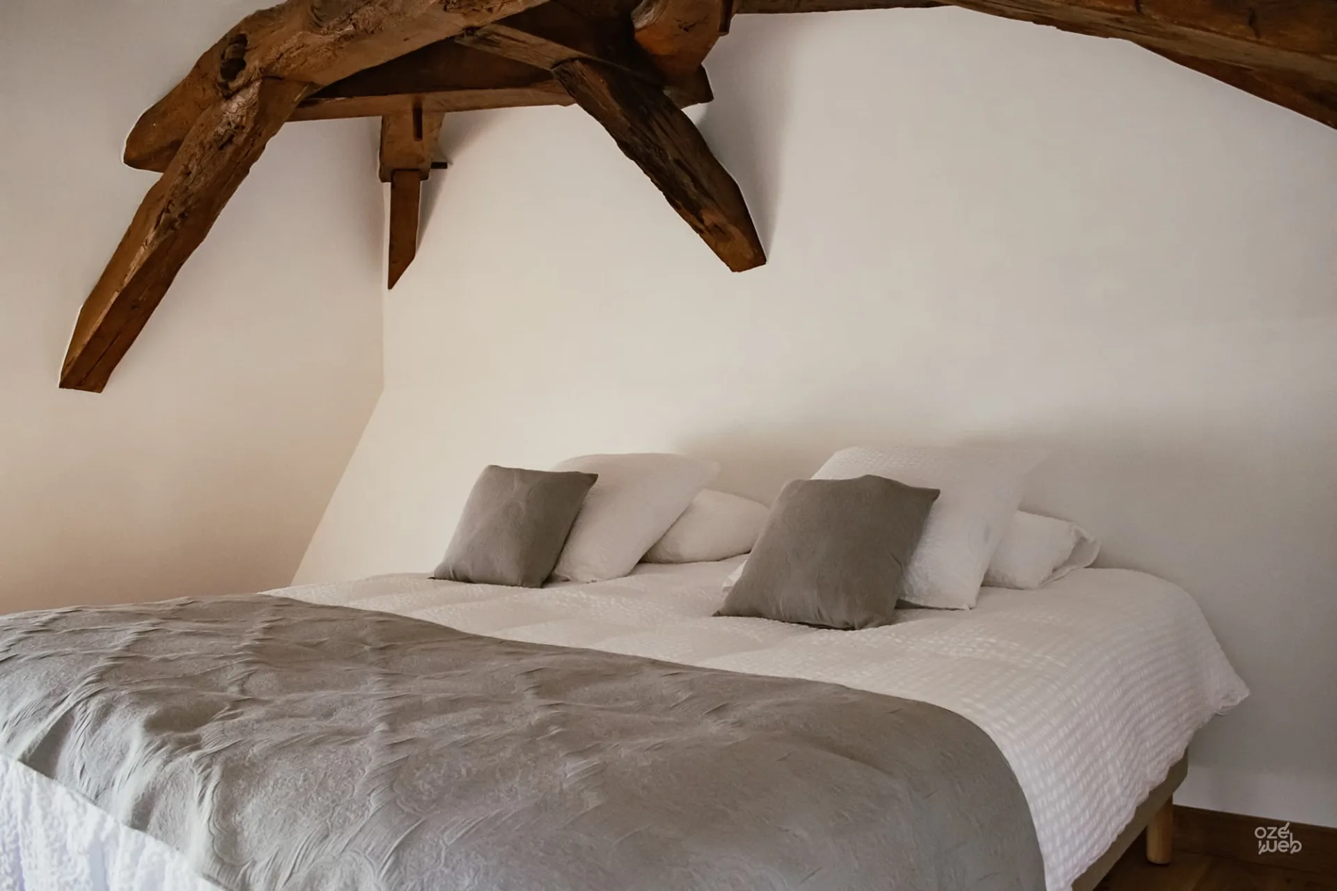 Deuxième chambre mansardée avec poutres et literie grise et blanche