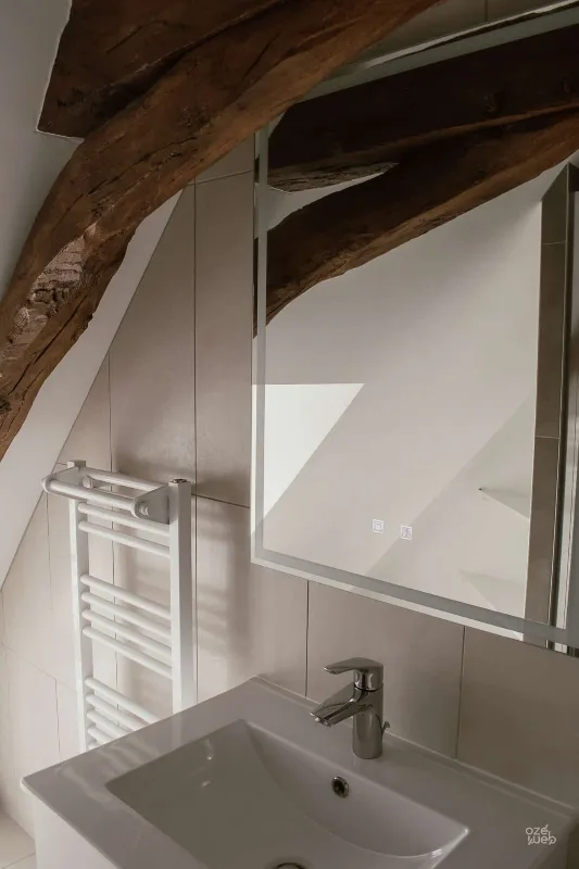 Salle de bain sous combles avec sèche-serviettes et charpente en bois brut