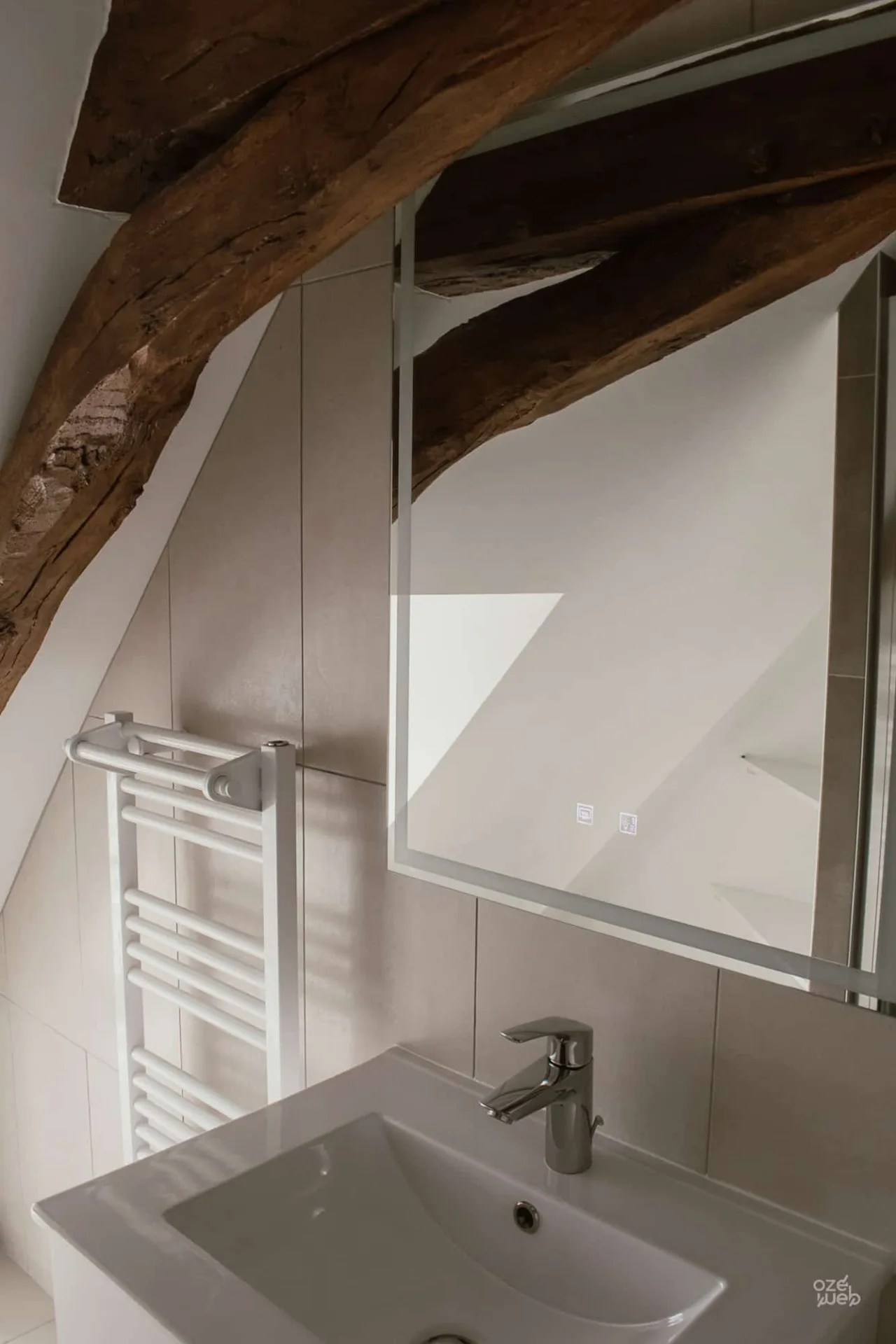 Salle de bain sous combles avec sèche-serviettes et charpente en bois brut