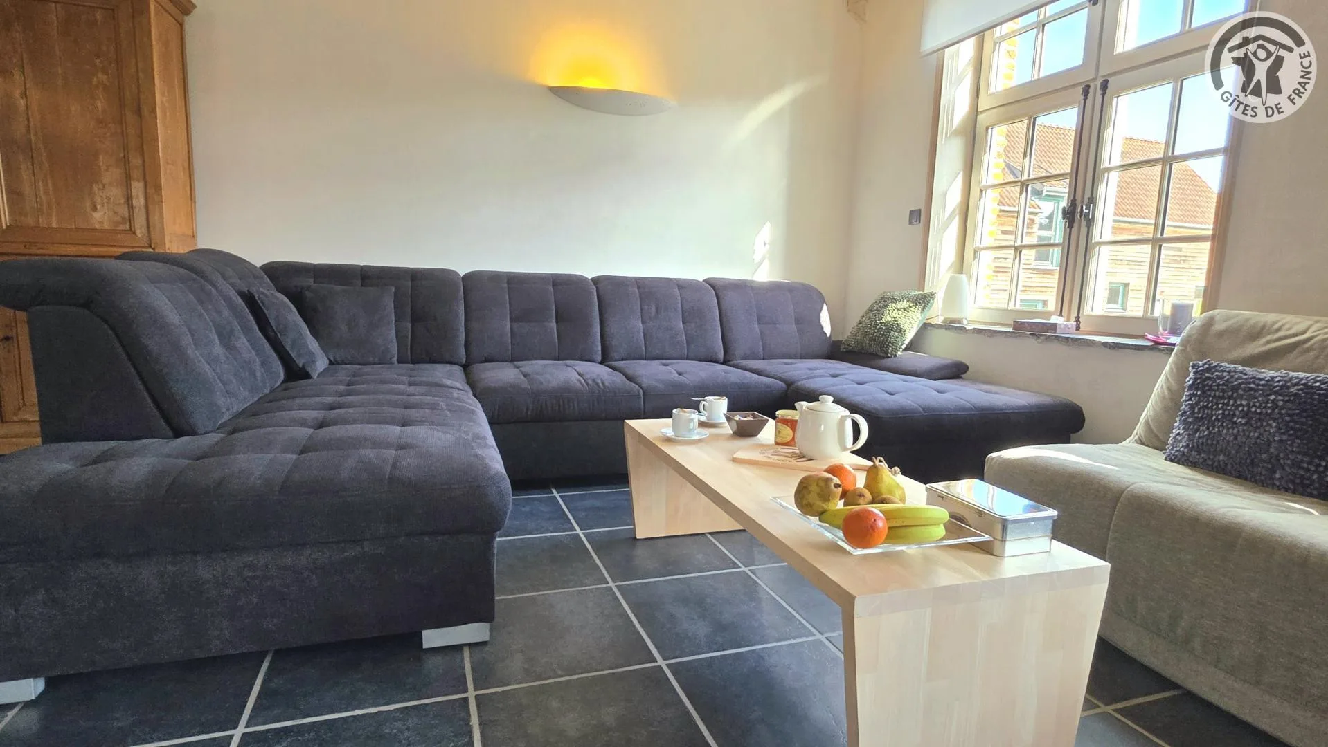 Salon avec canapé d'angle gris et vue sur fenêtres à petits carreaux