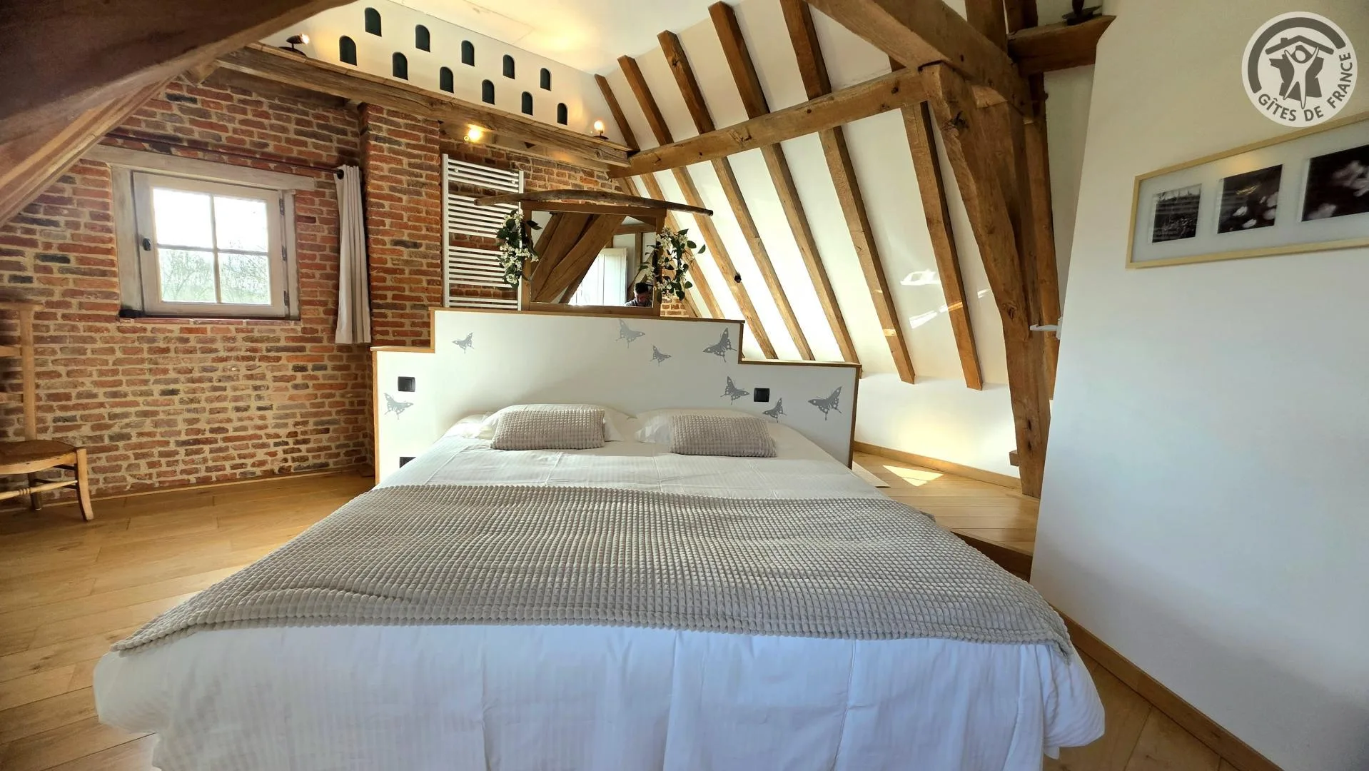 Chambre sous combles avec mur en brique apparente, poutres et lit double
