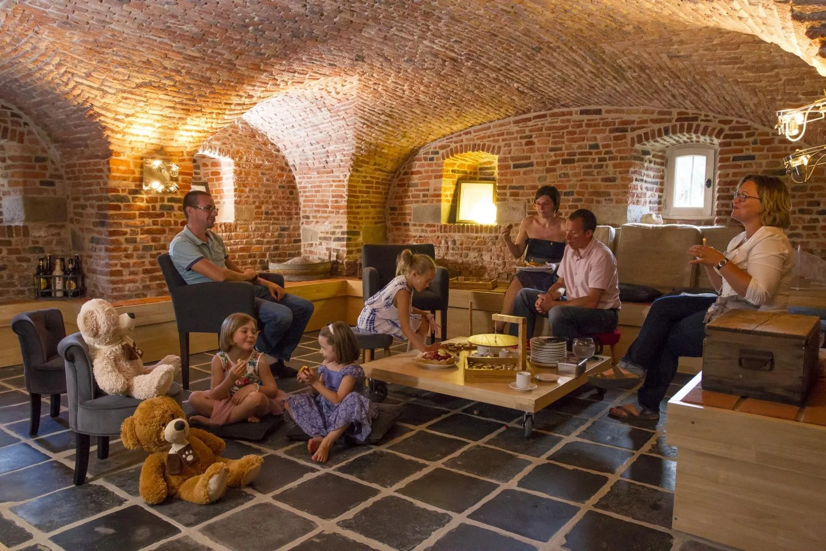 Cave voûtée en briques aménagée en espace convivial, famille réunie autour d'une table basse