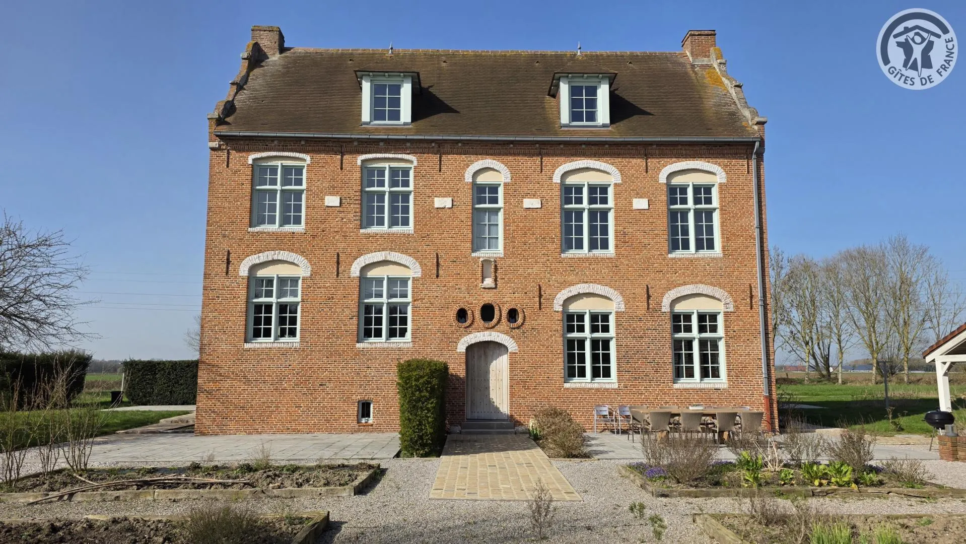 Gîte de groupe Le Manoir du Bolgaro à Morbecque — Façade en briques du Manoir du Bolgaro avec terrasse et table dressée en extérieur, capacité 12 personnes