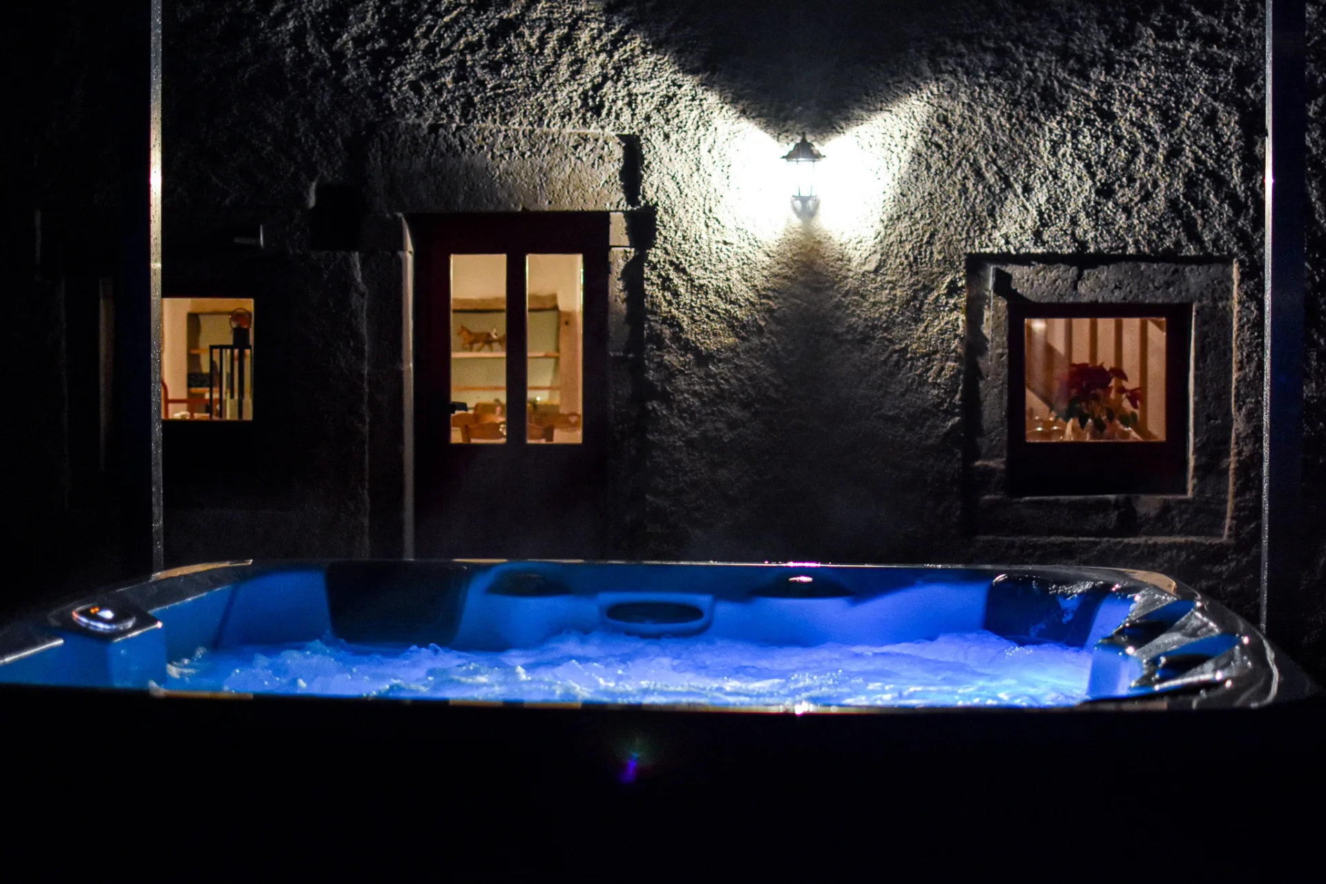 Spa extérieur illuminé en bleu la nuit devant la façade en pierre