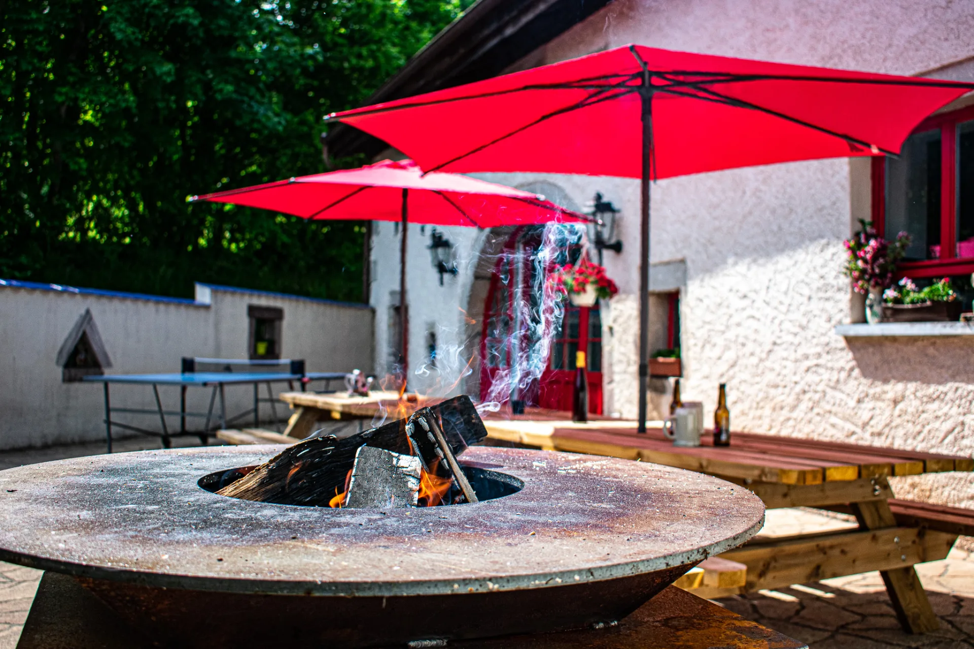 Terrasse avec brasero, umbrellas rouges et table de ping-pong devant la façade