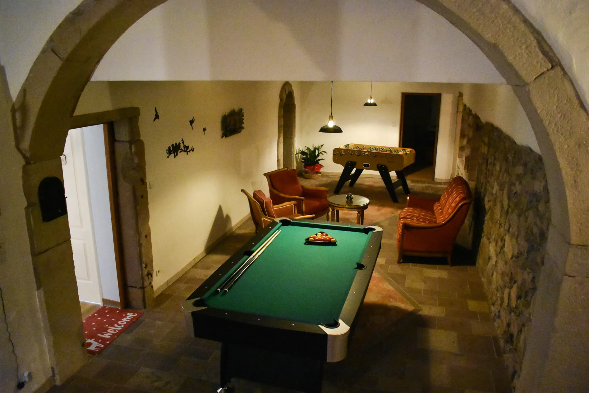 Salle de billard voûtée en pierre avec fauteuils et babyfoot