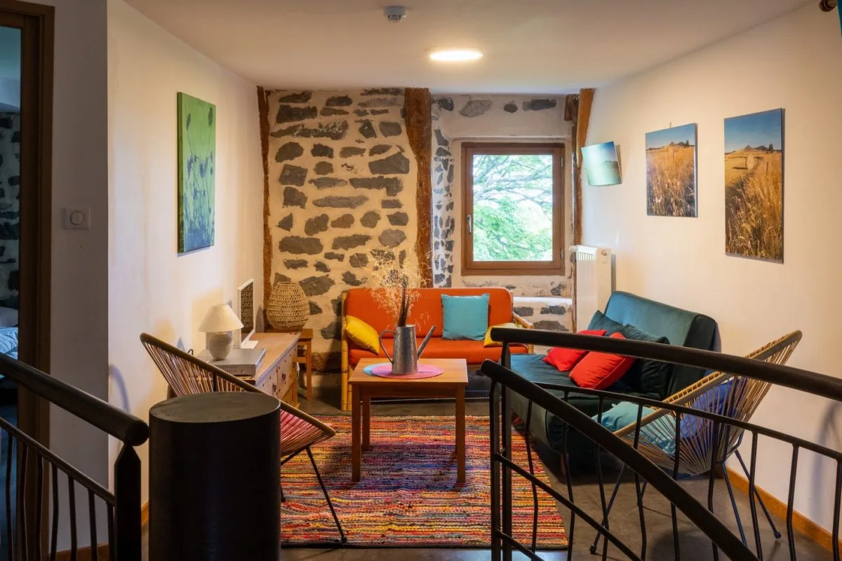 Salon à l'étage avec banquettes colorées et murs en pierre apparente