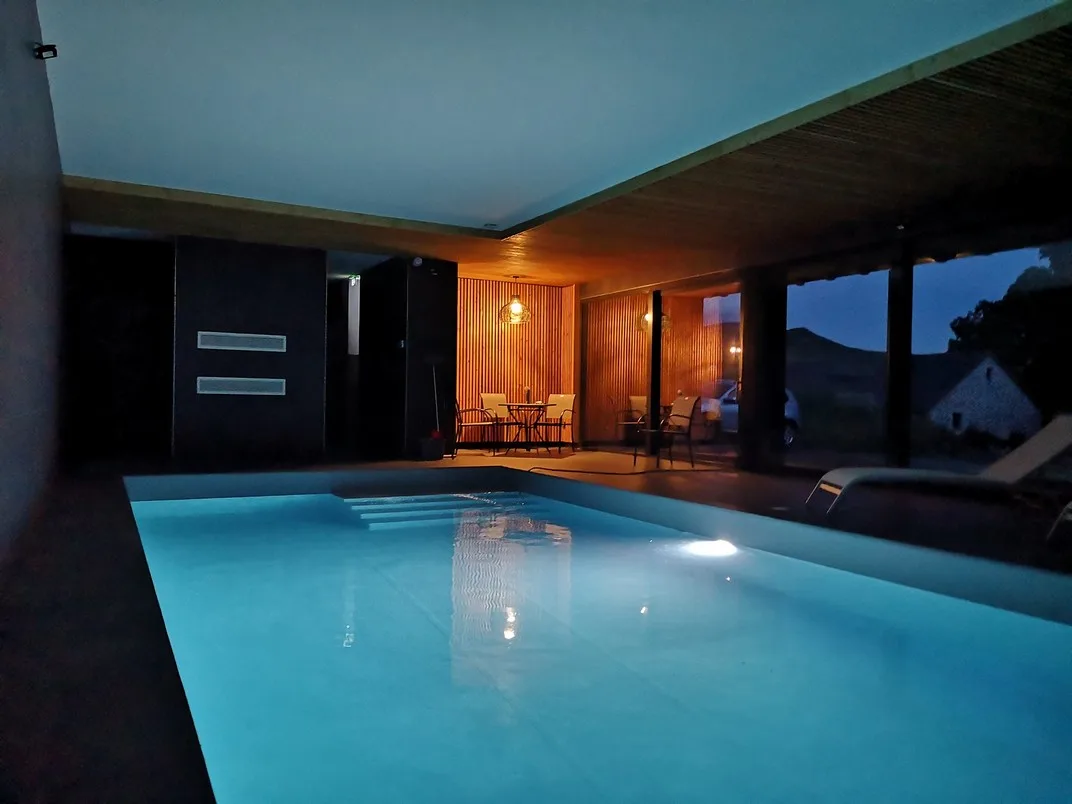 Piscine intérieure éclairée en soirée avec coin salon attenant