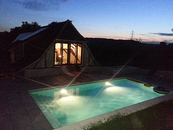 Piscine éclairée en soirée devant la véranda du gîte