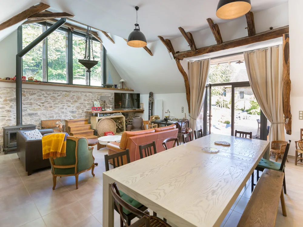 Salon avec poêle à bois et grande baie vitrée, poutres apparentes