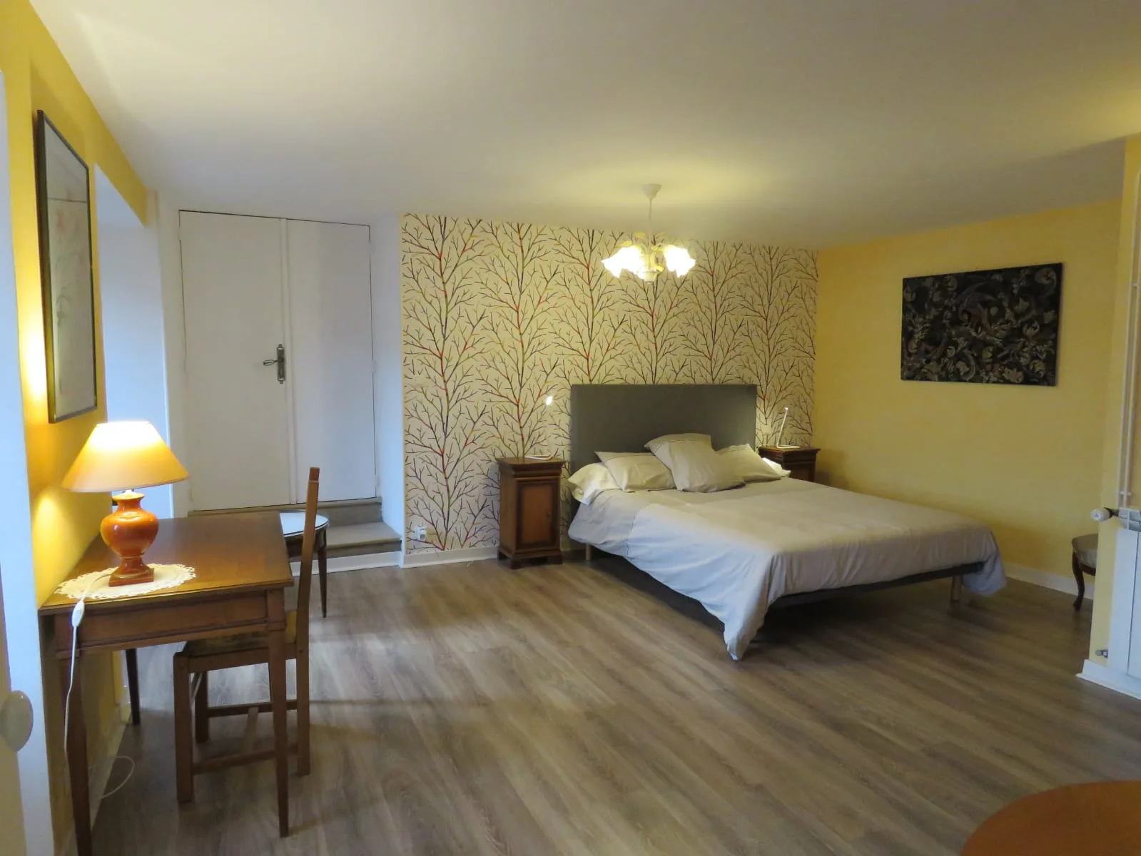 Chambre lumineuse aux murs jaunes, papier peint à motifs d'arbres et grand lit double