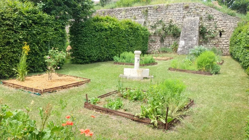 Jardin potager clos avec ancienne fontaine en pierre et parterres de légumes et fleurs