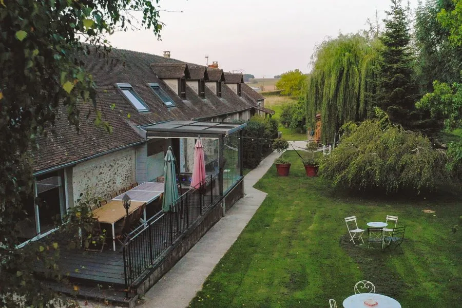 Gîte de groupe Ferme historique de Jean de la Fontaine à Chierry — Vue aérienne de la ferme en pierre avec terrasse couverte, jardin arboré et grands saules pleureurs, capacité 65 personnes