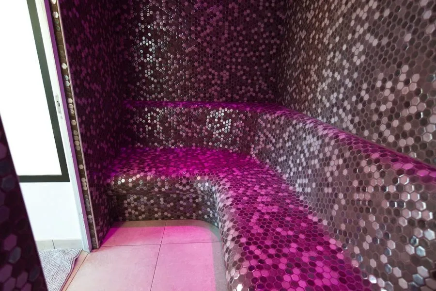 Hammam privatif en mosaïque violette avec éclairage d'ambiance et banquette