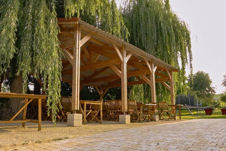Grande pergola en bois couverte avec tables et bancs, installée sous les saules pour les repas de groupe