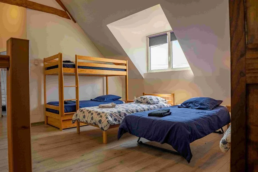 Chambre mansardée avec lit double, lits superposés en bois et velux sous charpente