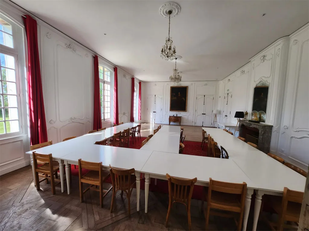 Grande salle de réception avec longue table dressée en blanc pouvant accueillir de nombreux convives