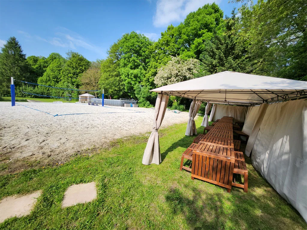 Grande tonnelle en bois installée dans le parc, avec tables et bancs pour les repas en extérieur
