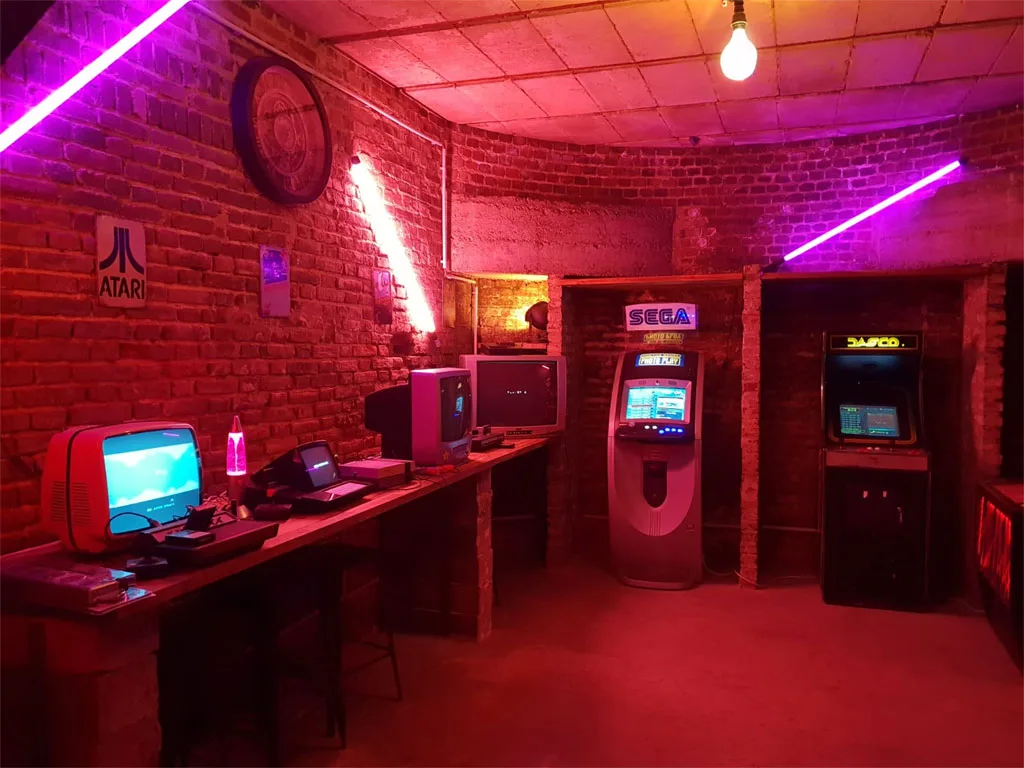 Coin jeux d'arcade avec néons roses, bornes lumineuses et mur en briques apparentes