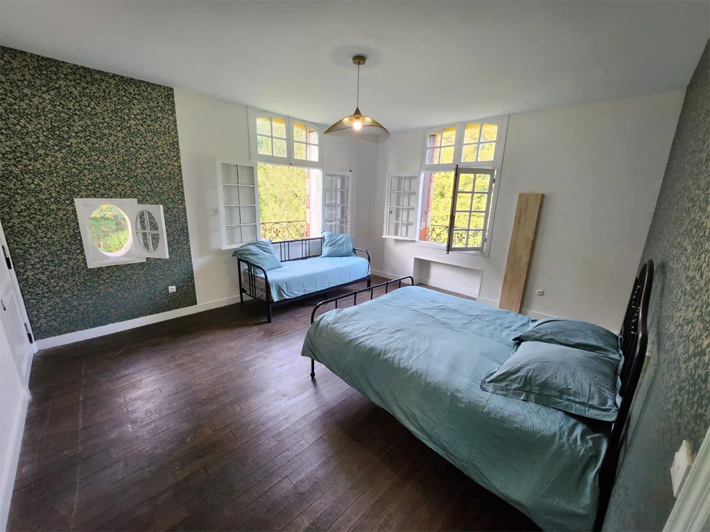 Chambre au papier peint vert à motifs, lit double et grandes fenêtres avec vue sur le parc