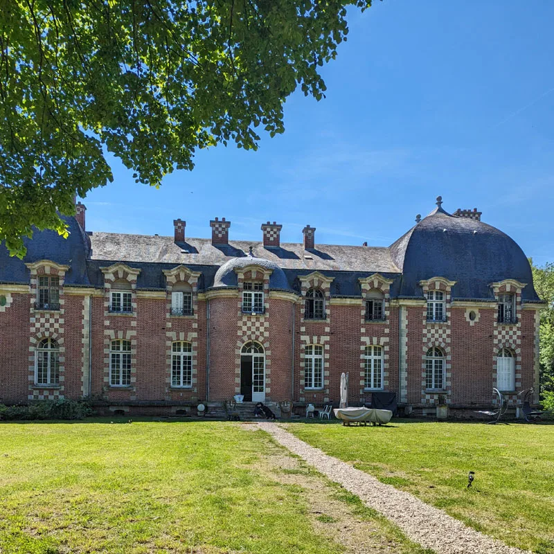 Vue d'ensemble de la façade du château depuis la pelouse, avec ses briques roses et ses hautes fenêtres