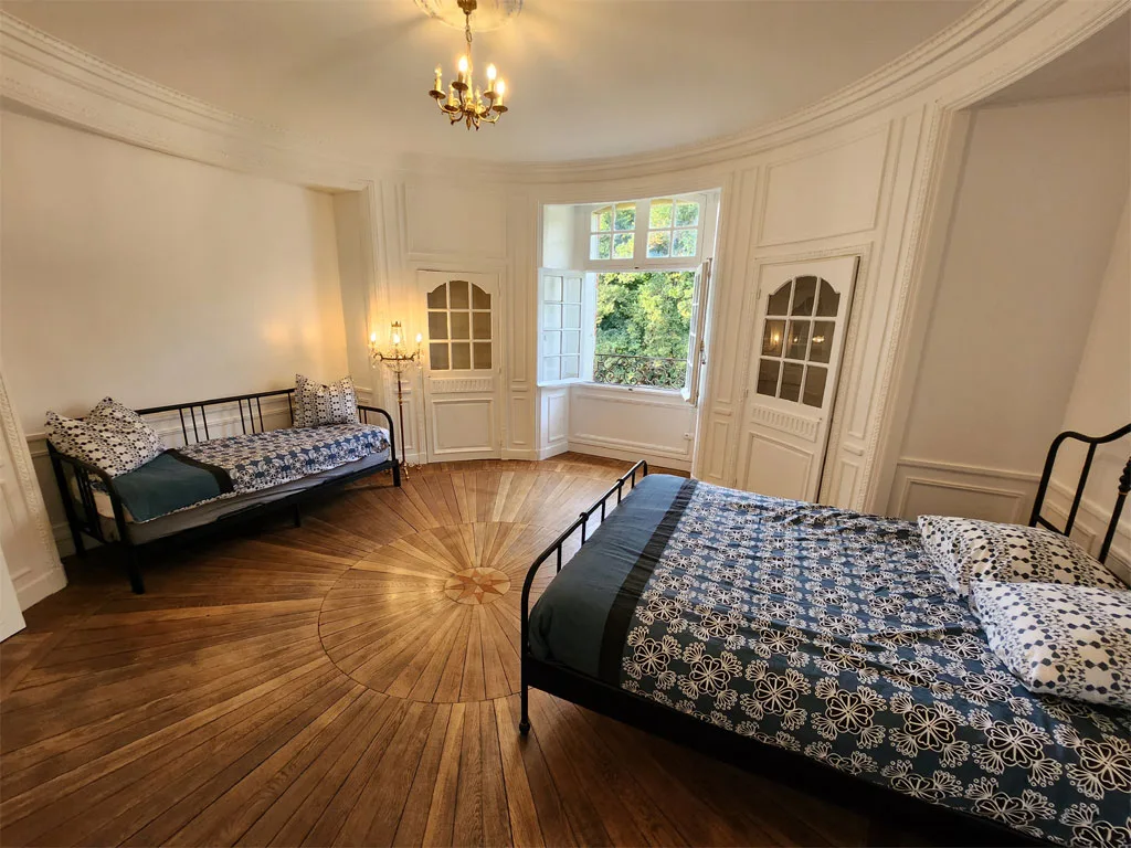 Chambre lumineuse avec deux lits doubles, parquet en bois et fenêtres à petits carreaux