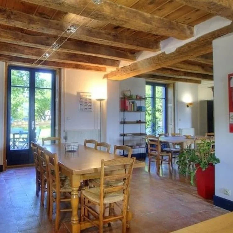 Salle à manger sous poutres apparentes avec deux grandes tables en bois pour les repas
