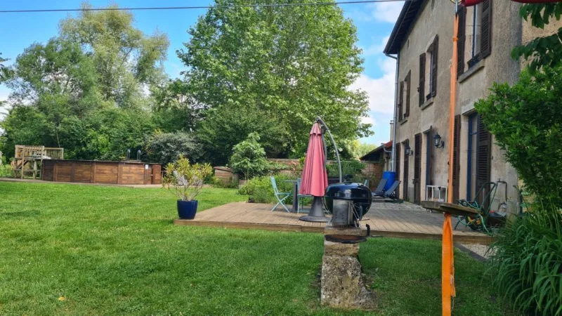 Terrasse en bois avec barbecue et salon de jardin, au bord de la pelouse
